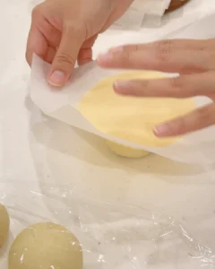 將菠蘿酥皮片連同烘焙紙蓋在麵團上